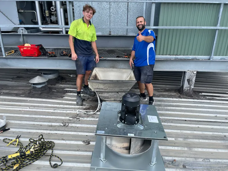 RAMCO team beside a rooftop exhaust fan and commercial ductwork